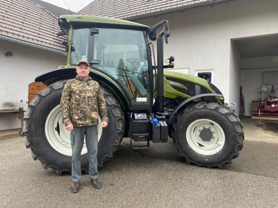 Mann steht neben grünem Valtra-Traktor im Hof eines Bauernhofs