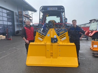 Gelbe Forstseilwinde 70MH pro am Traktor, zwei Monteure vor der Werkstatt bei der Übergabe