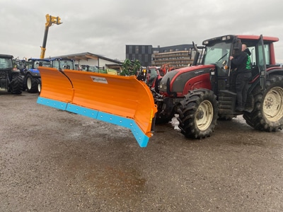 Traktor mit großem Schneepflug auf nassem Hof, Winterdienst Fahrzeug im Einsatz