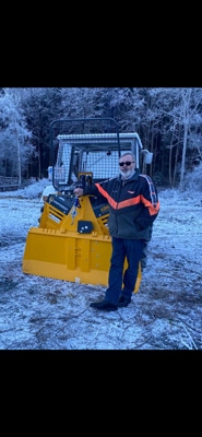 Person neben gelber Forstseilwinde vor Forstmaschine im winterlichen Wald