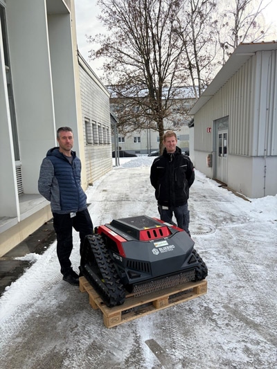 Zwei Personen neben Energreen RoboEVO Raupenmulcher auf Palette im verschneiten Industriegelände