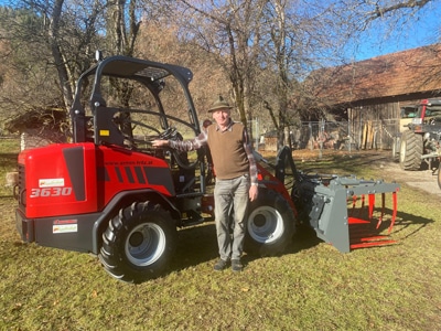 Mann neben rotem Hoflader 3630 mit Greifzange vor Scheune auf Bauernhof
