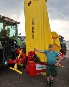 Ein Mann steht neben einem Pöttinger Mähwerk in Transportstellung an einem Traktor