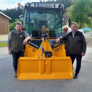 Zwei Männer stehen neben einer gelben Uniforest 60Hpro Forstseilwinde an einem Traktor