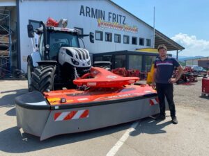 Ein Mann steht neben einem Steyr-Traktor mit Kuhn-Frontmähwerk vor dem Gebäude von Armin Fritz Landtechnik