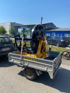 Gelbe Uniforest Forstmaschine auf einem Pongratz-Anhänger, gesichert mit einem Spanngurt
