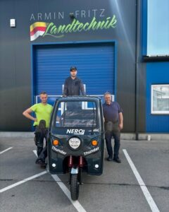 Drei Männer von Armin Fritz Landtechnik mit einem Nero Thunder Elektrofahrzeug vor dem Firmengebäude